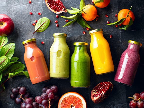 colourful smoothie drinks in glass bottles surrounded by fresh fruit 